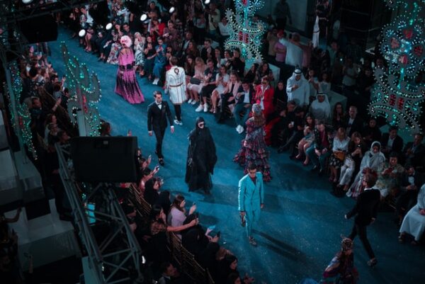 Models walking on a fashion show stage with the audience and lighted decorations lining the catwalk